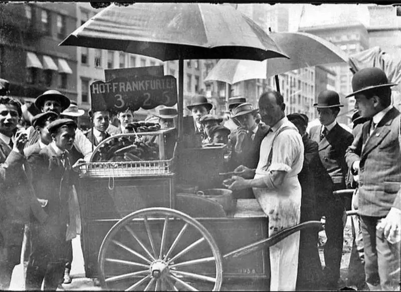 a busy new york city street scene in the 1910s with many hot dog carts.