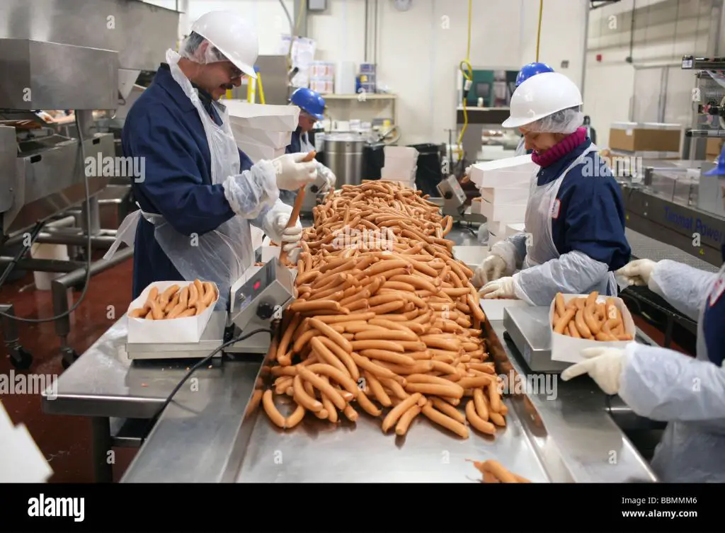 a factory worker monitoring hot dogs on a production line.