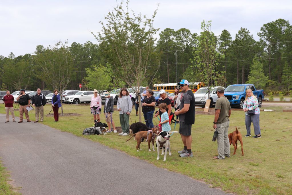 a group of people gathered at a dog park grand opening event.