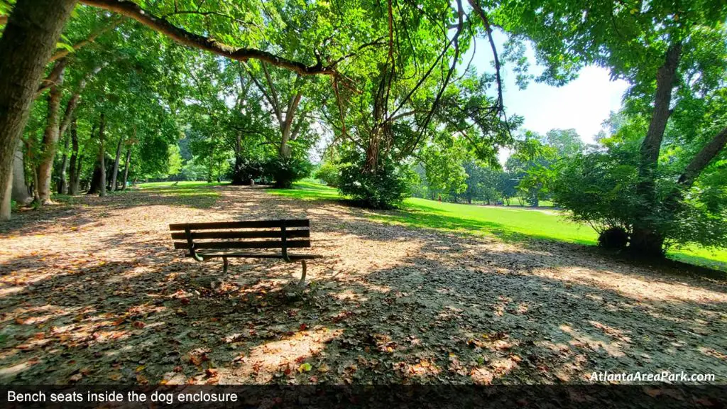 bench shaded by trees inside fenced dog park 