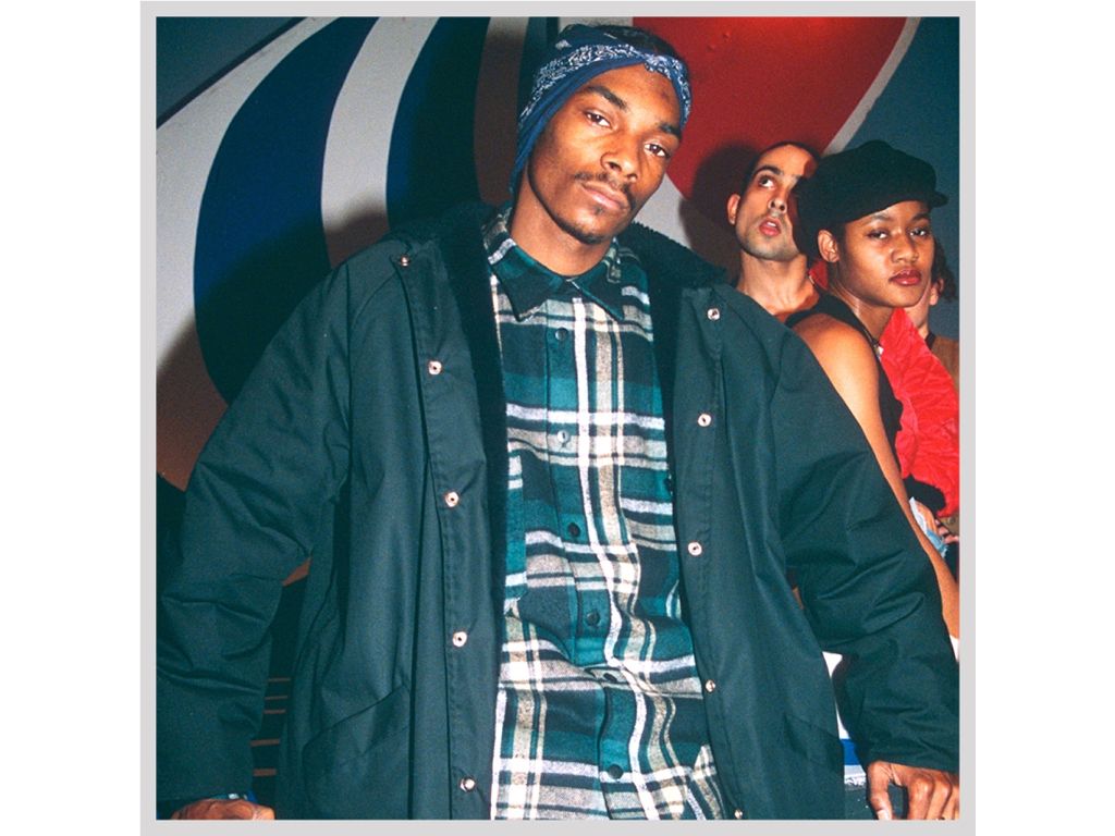 snoop dogg performing in the 90s, wearing braids, sunglasses, and a flannel shirt.